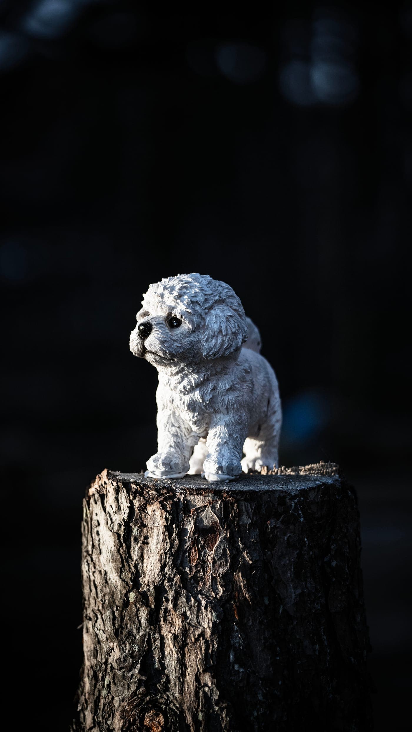 Hundfigurin i vitt porslin på en trästubbe mot mörk bakgrund